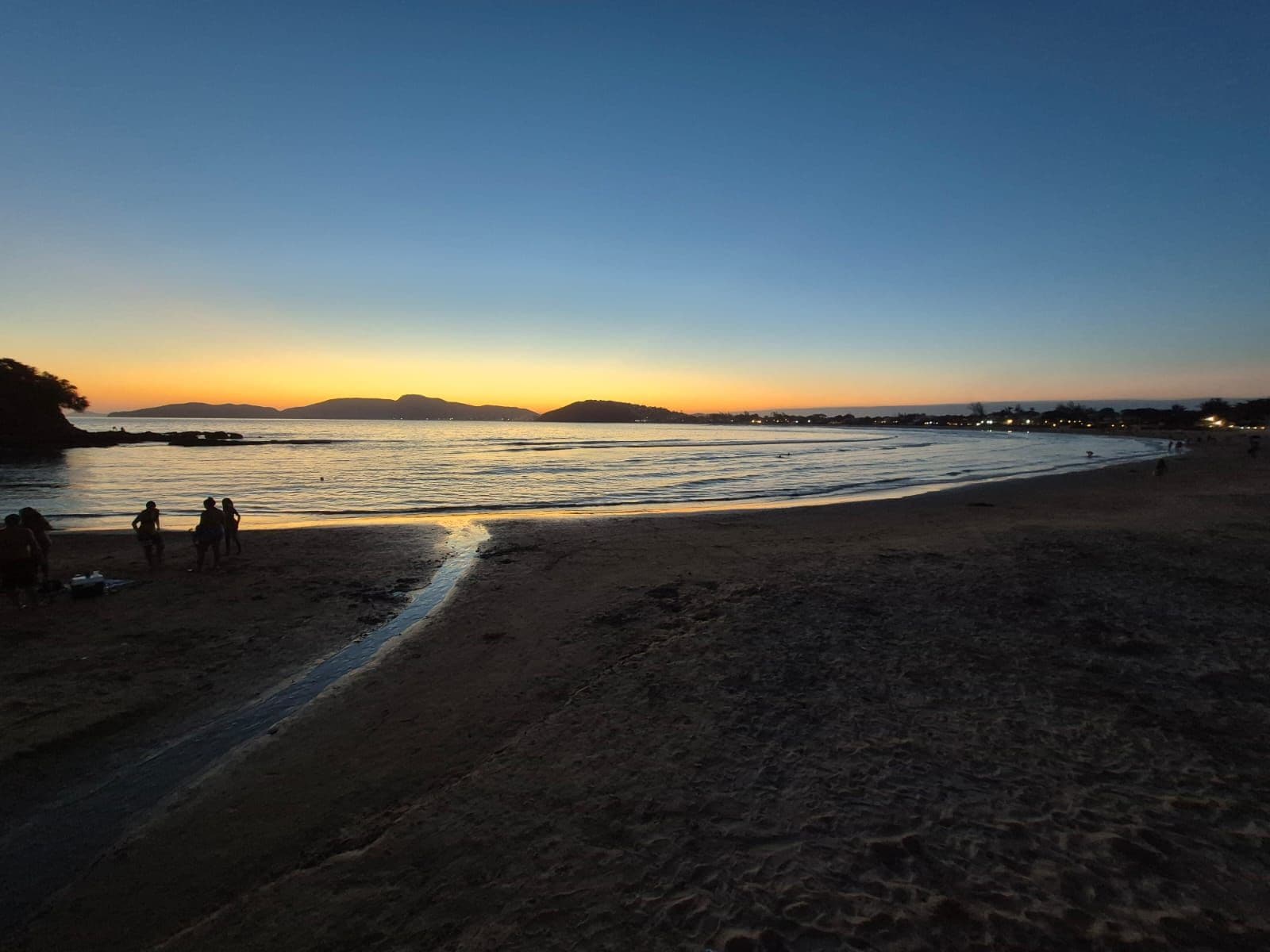 A beach at sunset with people walking along the shore.