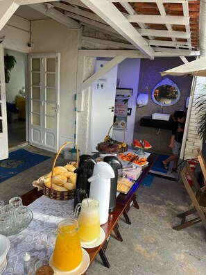 Ein reichhaltiges Buffet mit Brot, Gebäck und Getränken, ein Waschbecken und ein Spiegel in einem Raum mit Tür und Hinweisschild für eine Toilette.