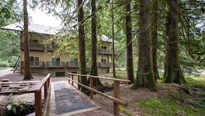 A wooden bridge leading to a multi-story building surrounded by tall trees. - Mt Baker Lodging Condo - Perfect for Smaller Families on the Go (Deming)