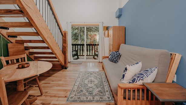 A wooden staircase leading to a balcony with a view of trees. A sofa and a small table are in the foreground. - Mt Baker Lodging Condo - Perfect for Smaller Families on the Go (Deming)