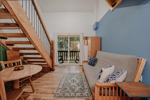 A wooden staircase leading to a balcony with a view of trees. A sofa and a small table are in the foreground. - Mt Baker Lodging Condo - Perfect for Smaller Families on the Go (Deming)