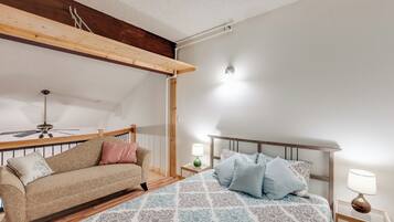 Un dormitorio con cama, sofá, ventilador de techo y mesita de noche con lámpara.