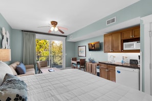 A bedroom with a bed, a desk, a chair, a ceiling fan, and a view of the outdoors.