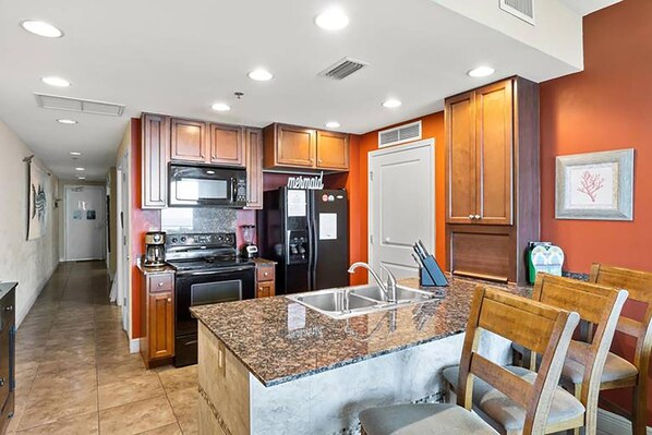 A modern kitchen with granite countertops, stainless steel appliances, and wooden cabinetry. - Sterling Breeze 1903 (Panama City Beach)