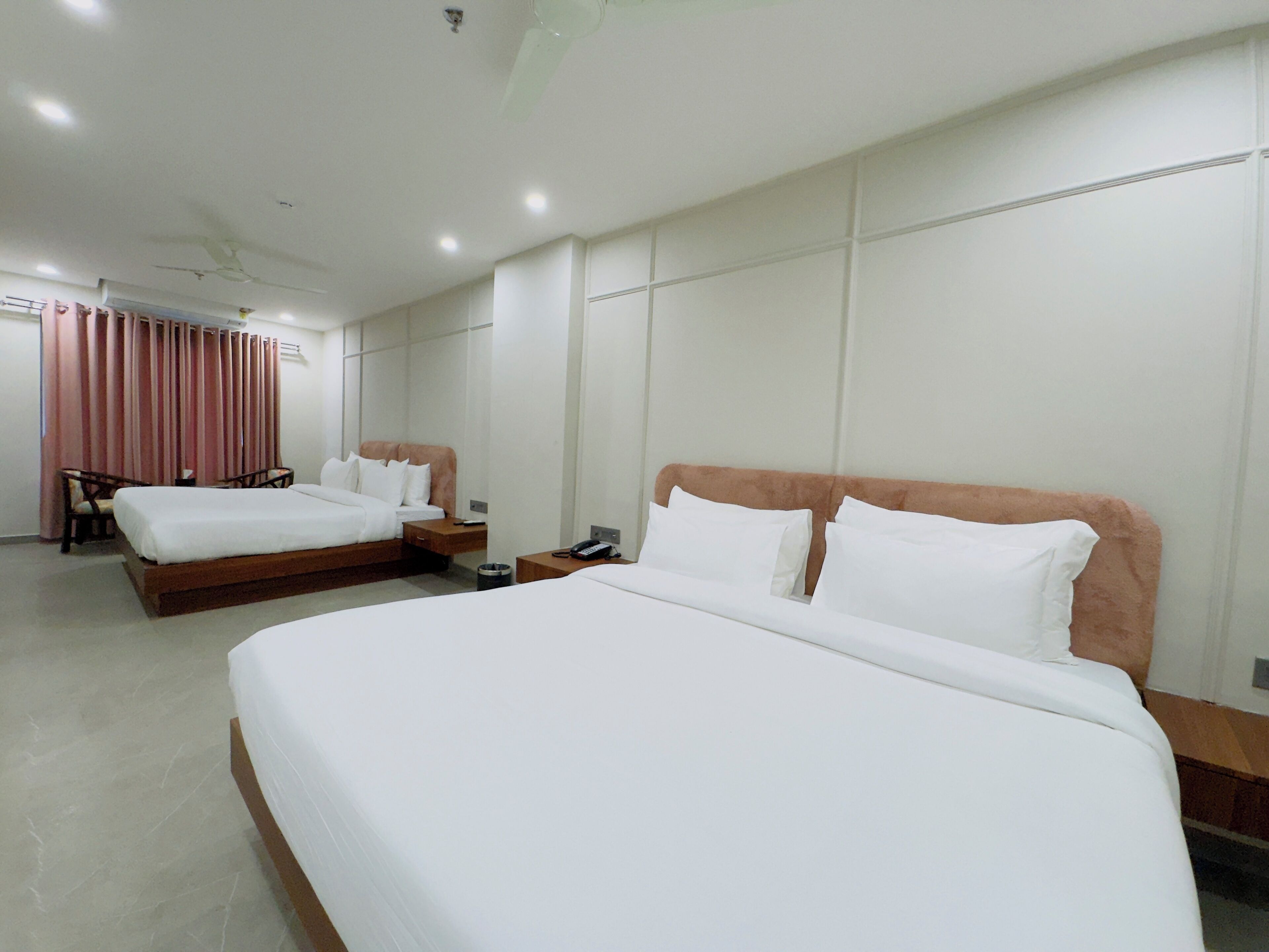 Quarto de hotel com duas camas, uma escrivaninha, uma cadeira e um ventilador de teto.