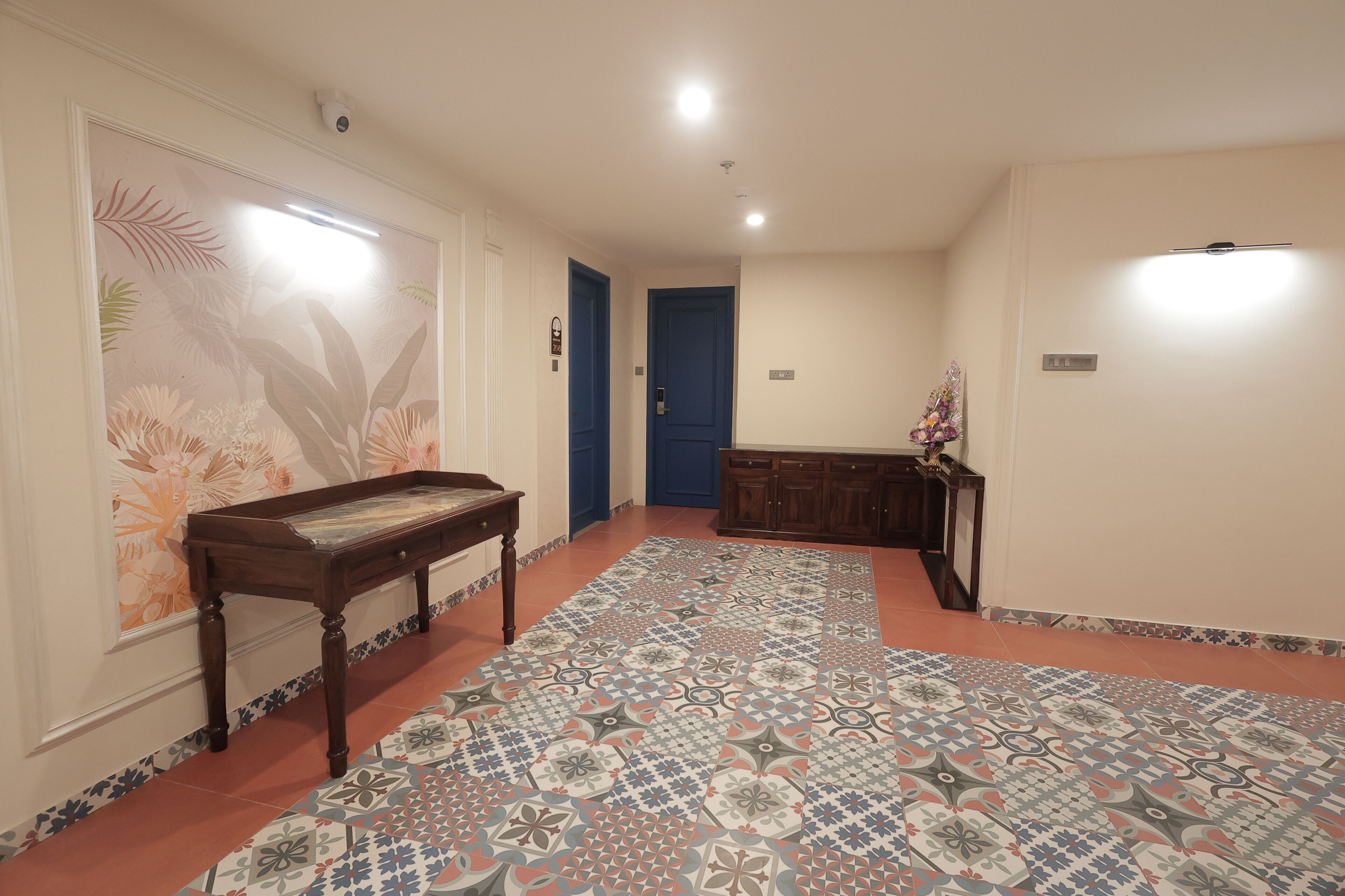 A hallway with patterned flooring, a wooden bench, a blue door, and a small table with a vase.