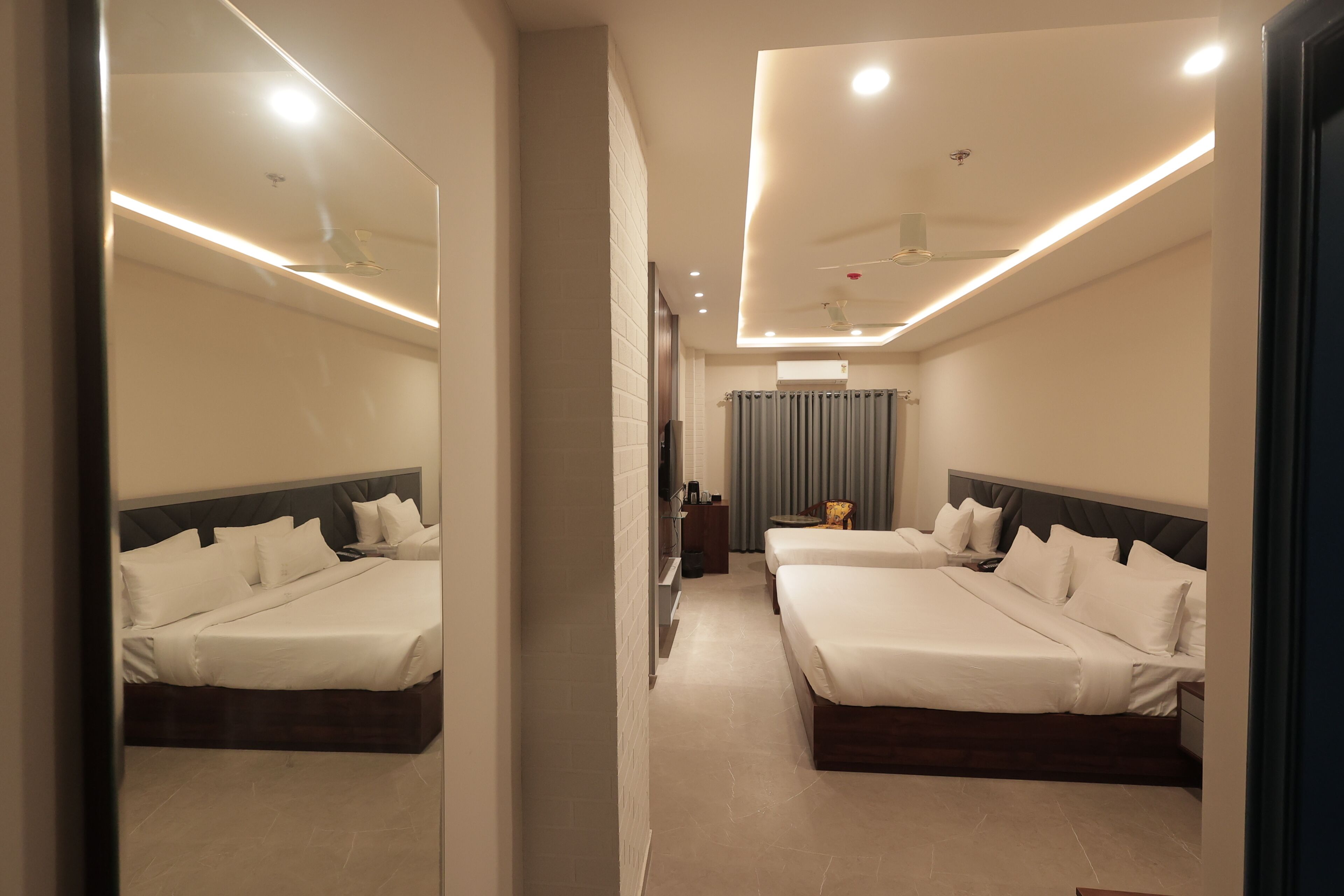 A hotel room with two beds, a mirror, a ceiling fan, and a TV.