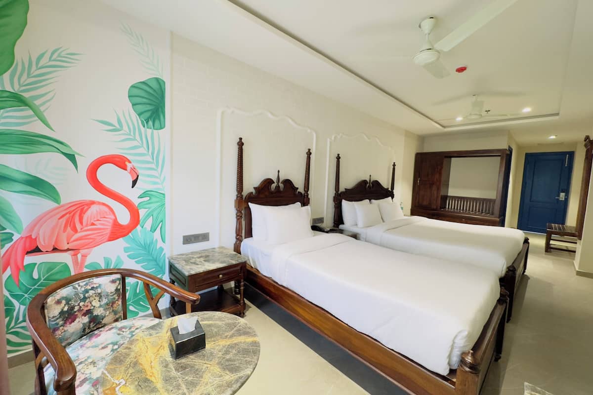 Une chambre d’hôtel avec un grand lit, une tête de lit en bois, une petite table ronde et une fresque murale représentant un flamant rose.