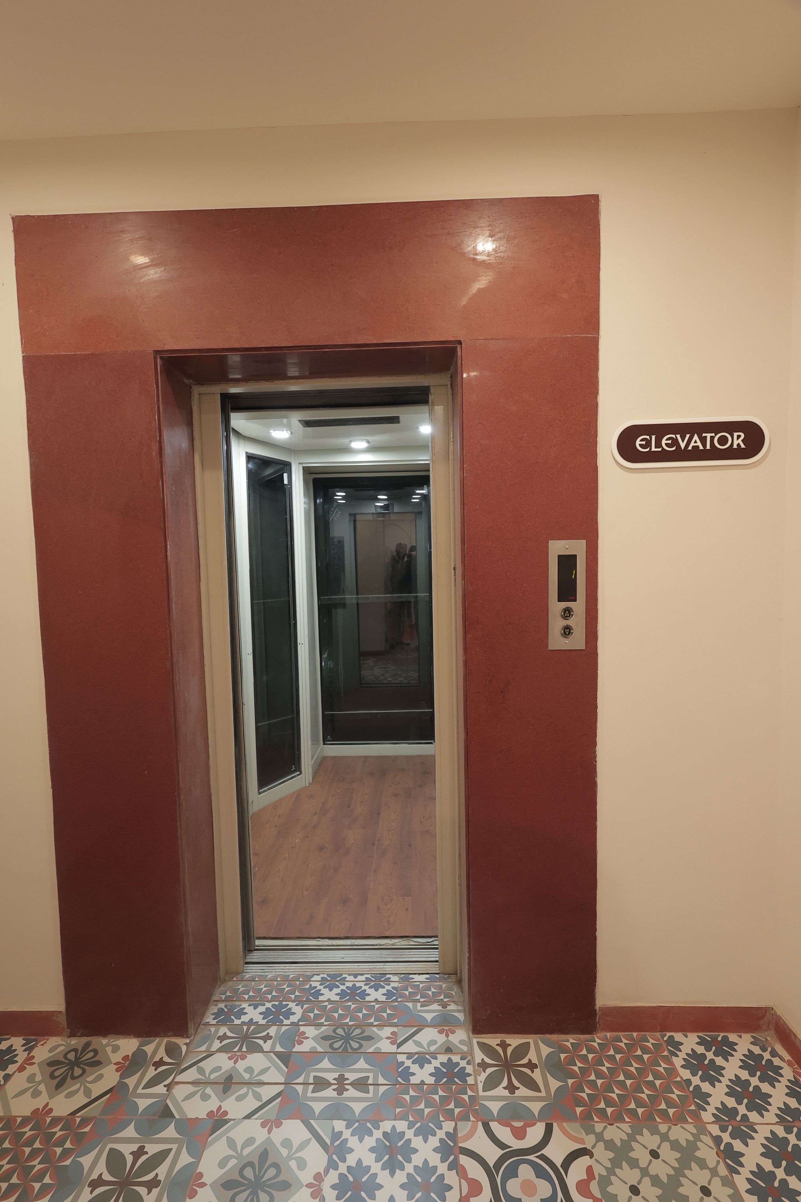 An elevator with a sign, a patterned floor, and a red wall.