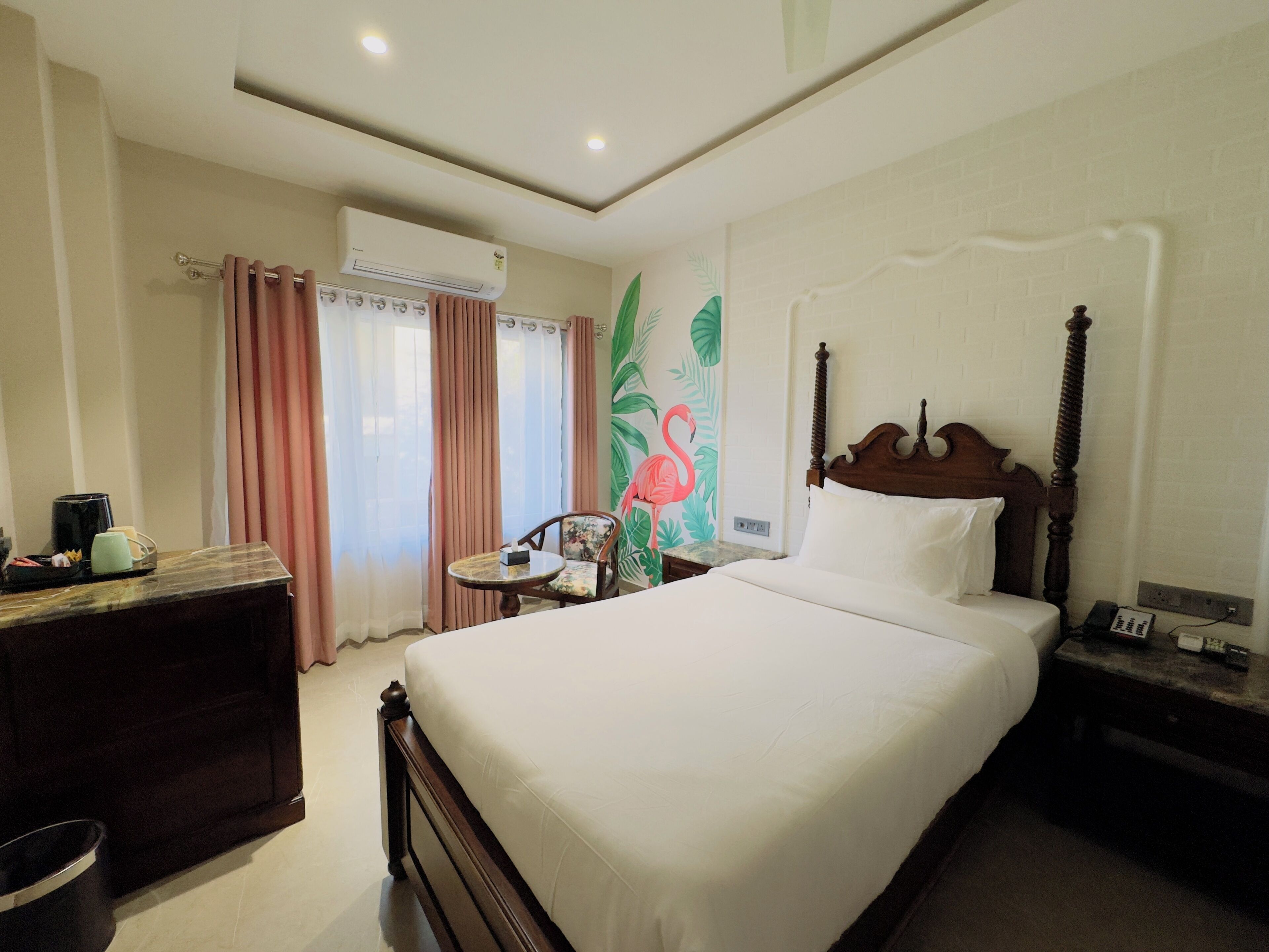Quarto de hotel com cama, escrivaninha, cadeira, ar condicionado e parede com mural floral.