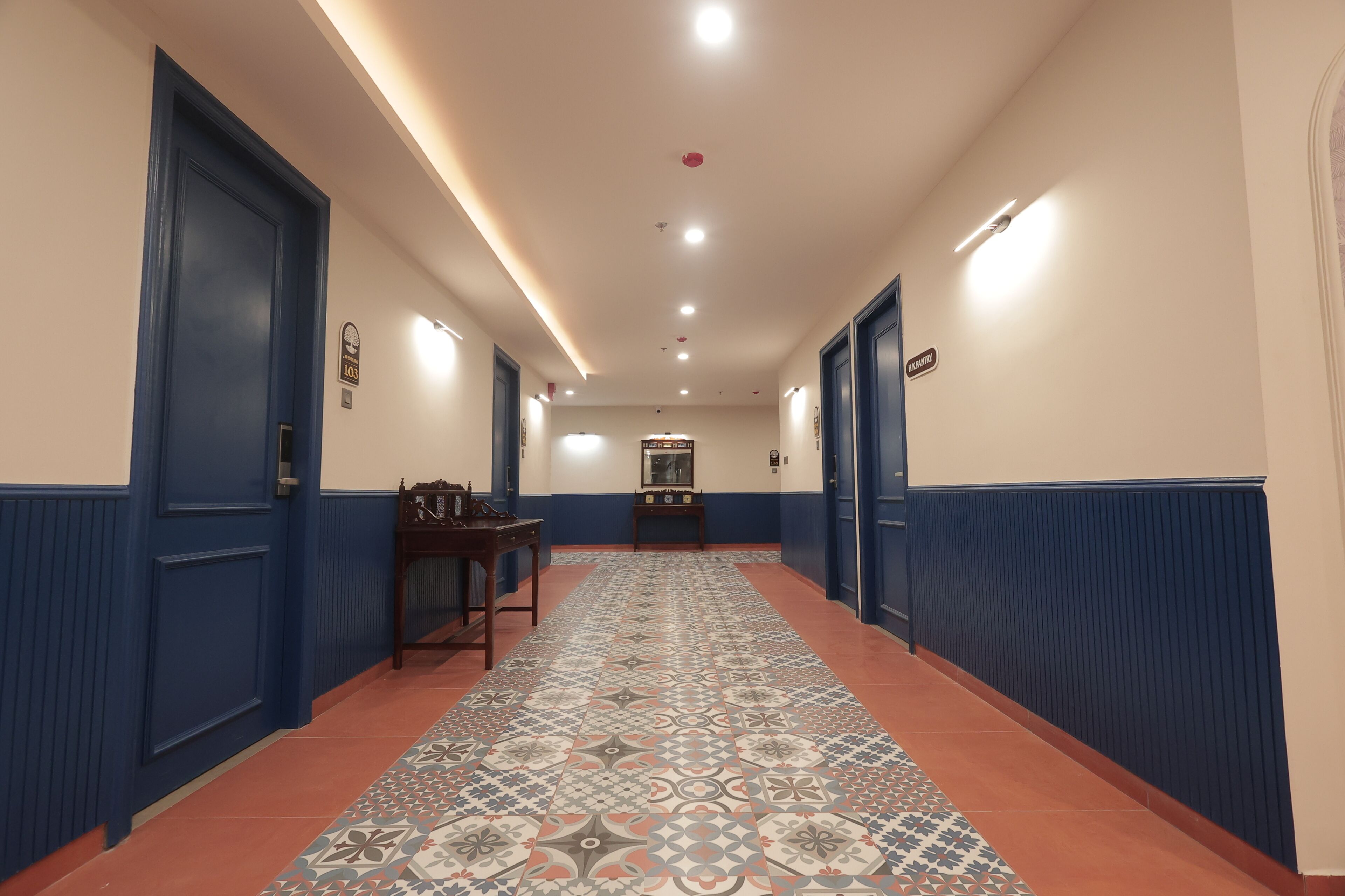 A hotel hallway with blue doors, a patterned carpet, and a central bench.