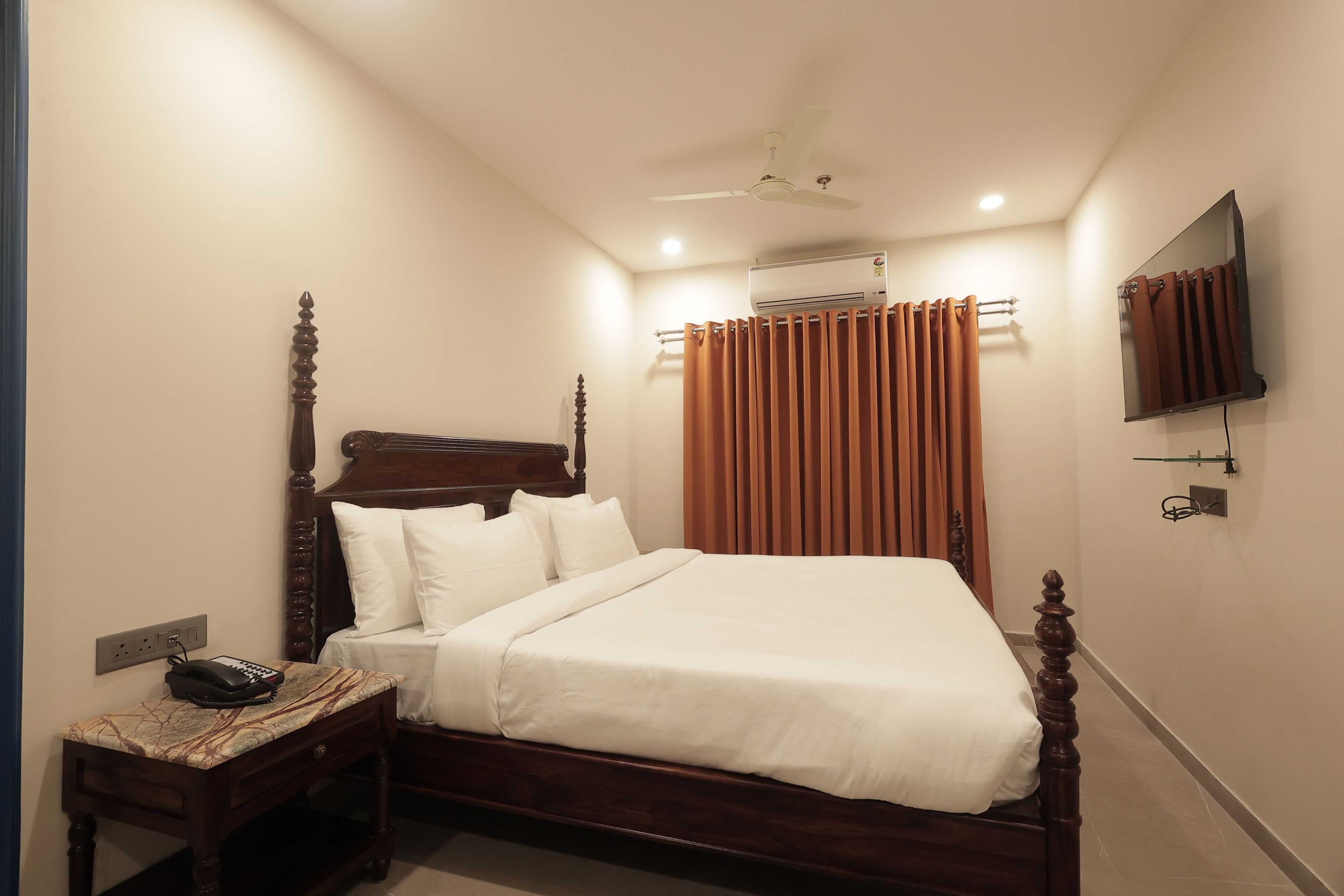 Una cama bien hecha con cabecera de madera, una mesita de noche con un teléfono y un aire acondicionado instalado en la pared.
