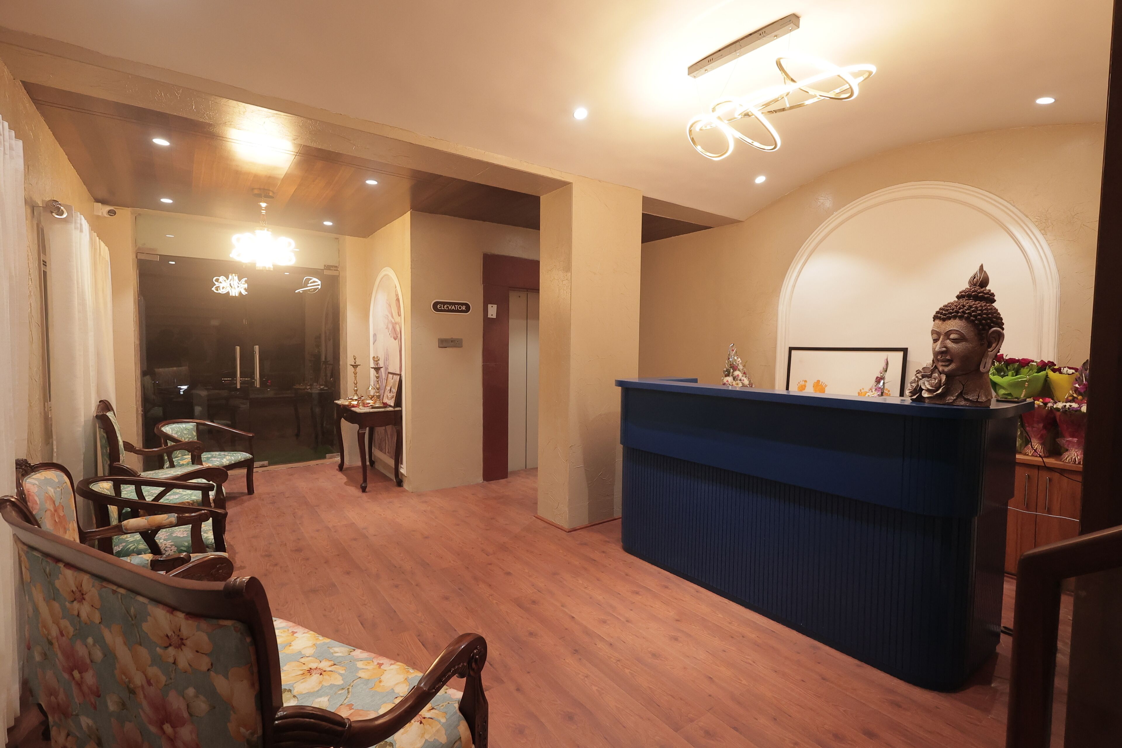 A reception area with a blue counter, wooden chairs, and a Buddha statue.