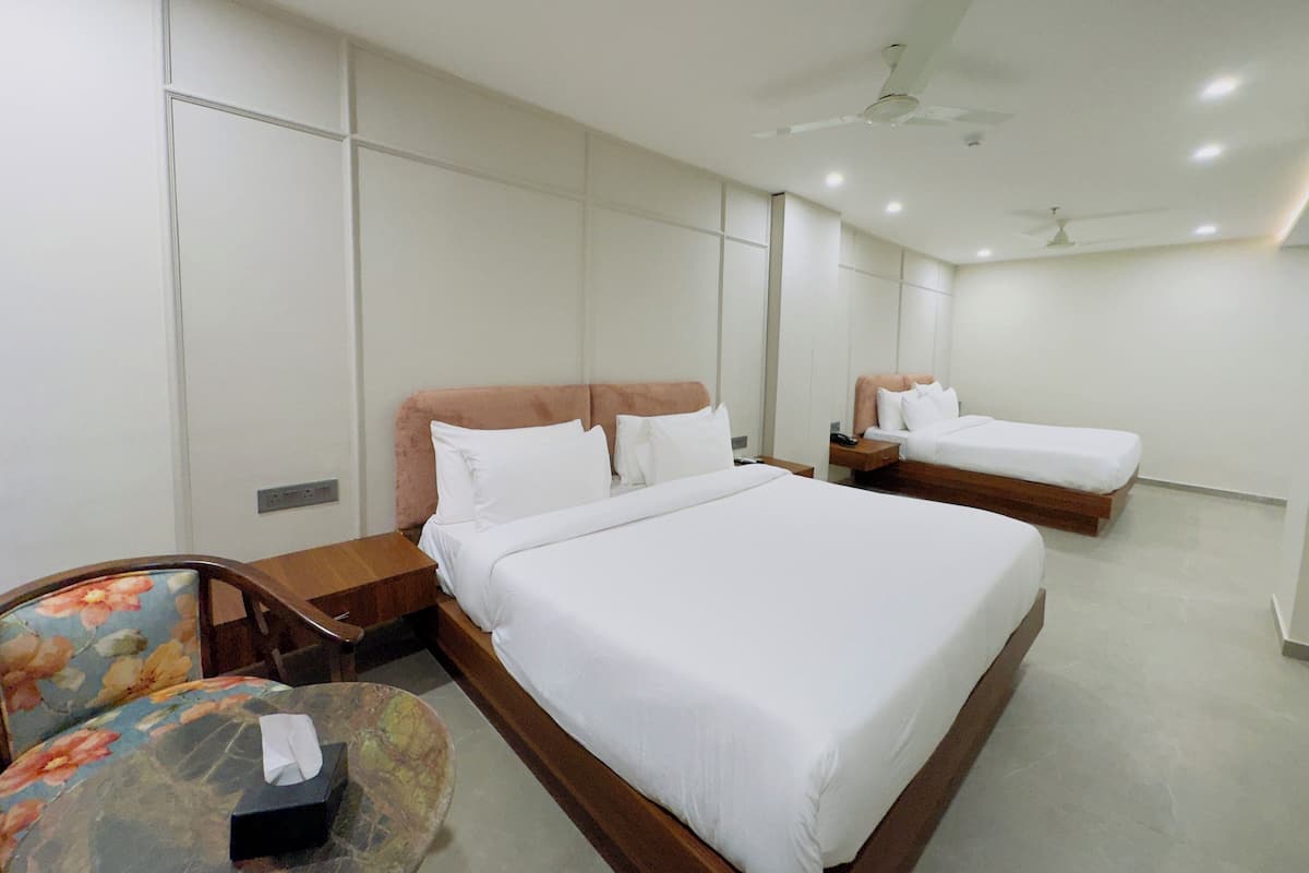 Une chambre d’hôtel avec deux lits, une tête de lit en bois, une chaise à motifs floraux et un ventilateur de plafond.