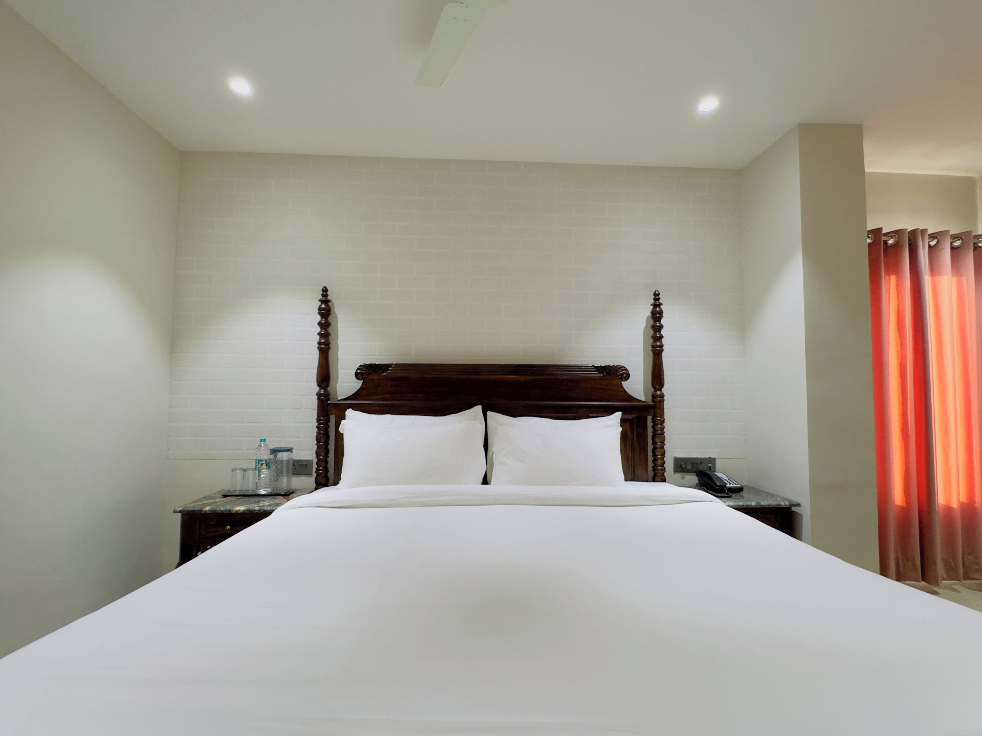 Une chambre d’hôtel avec un grand lit, une tête de lit en bois, une table de chevet avec un téléphone et un rideau rouge.