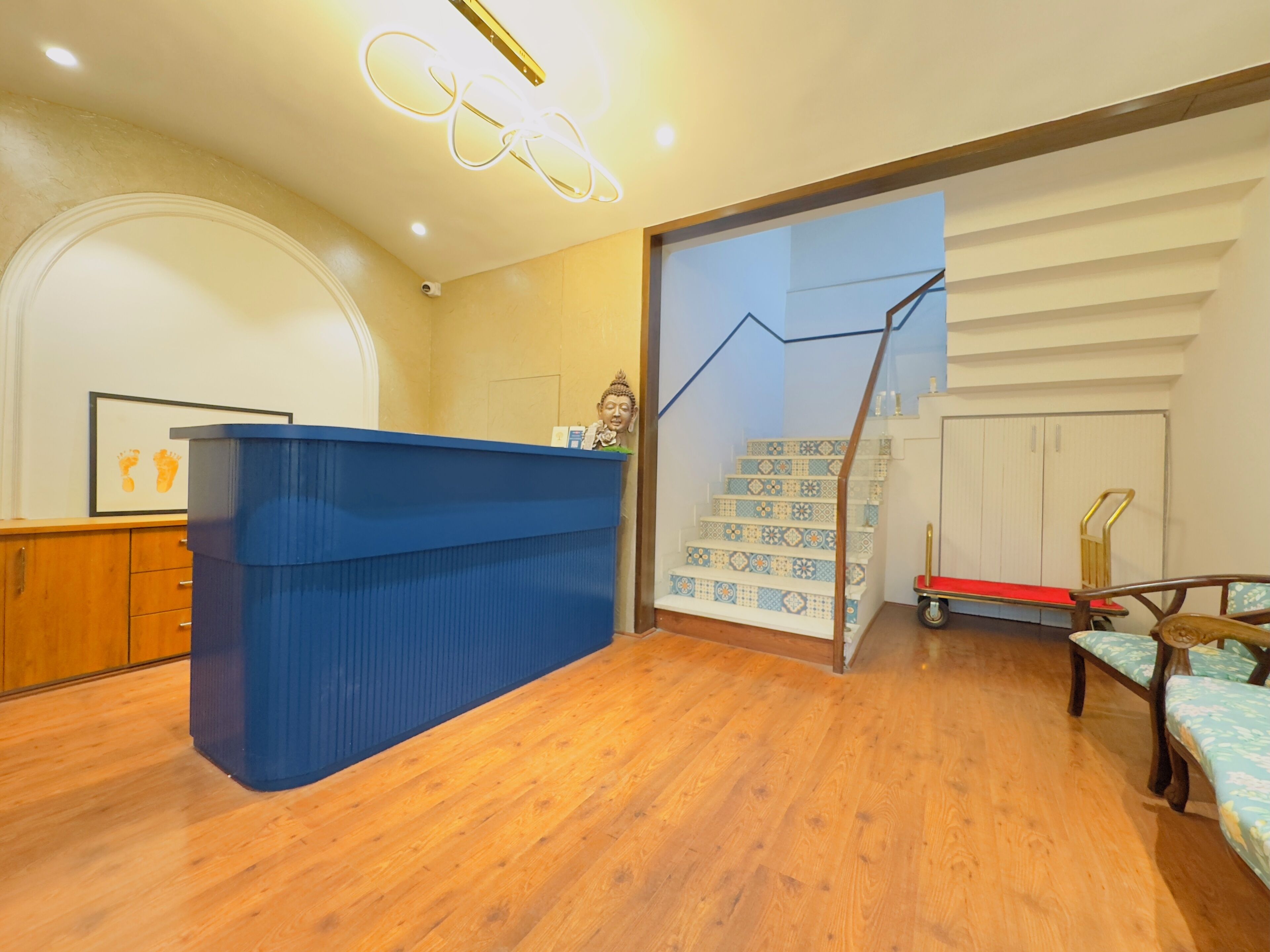 A reception area with a blue counter, wooden flooring, a staircase with patterned tiles, and a small cart.