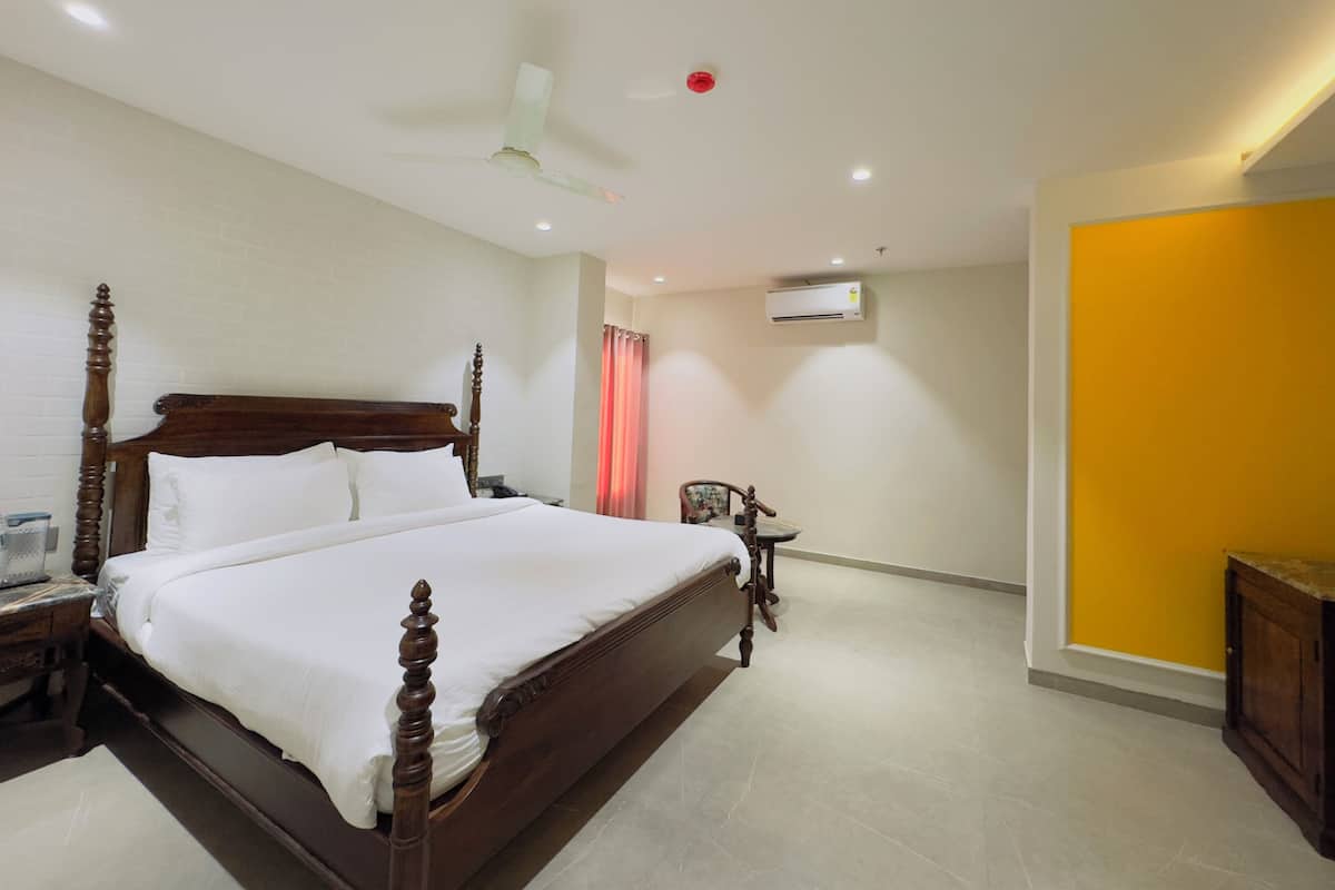 Une chambre spacieuse avec un grand lit, un ventilateur de plafond, un appareil de climatisation et une petite table avec une chaise.