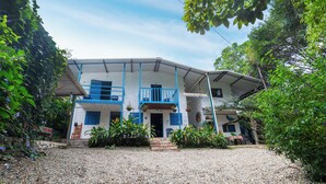A two-story building with a balcony, surrounded by greenery and a gravel driveway. - La Posada De Las Aves (San Rafael)