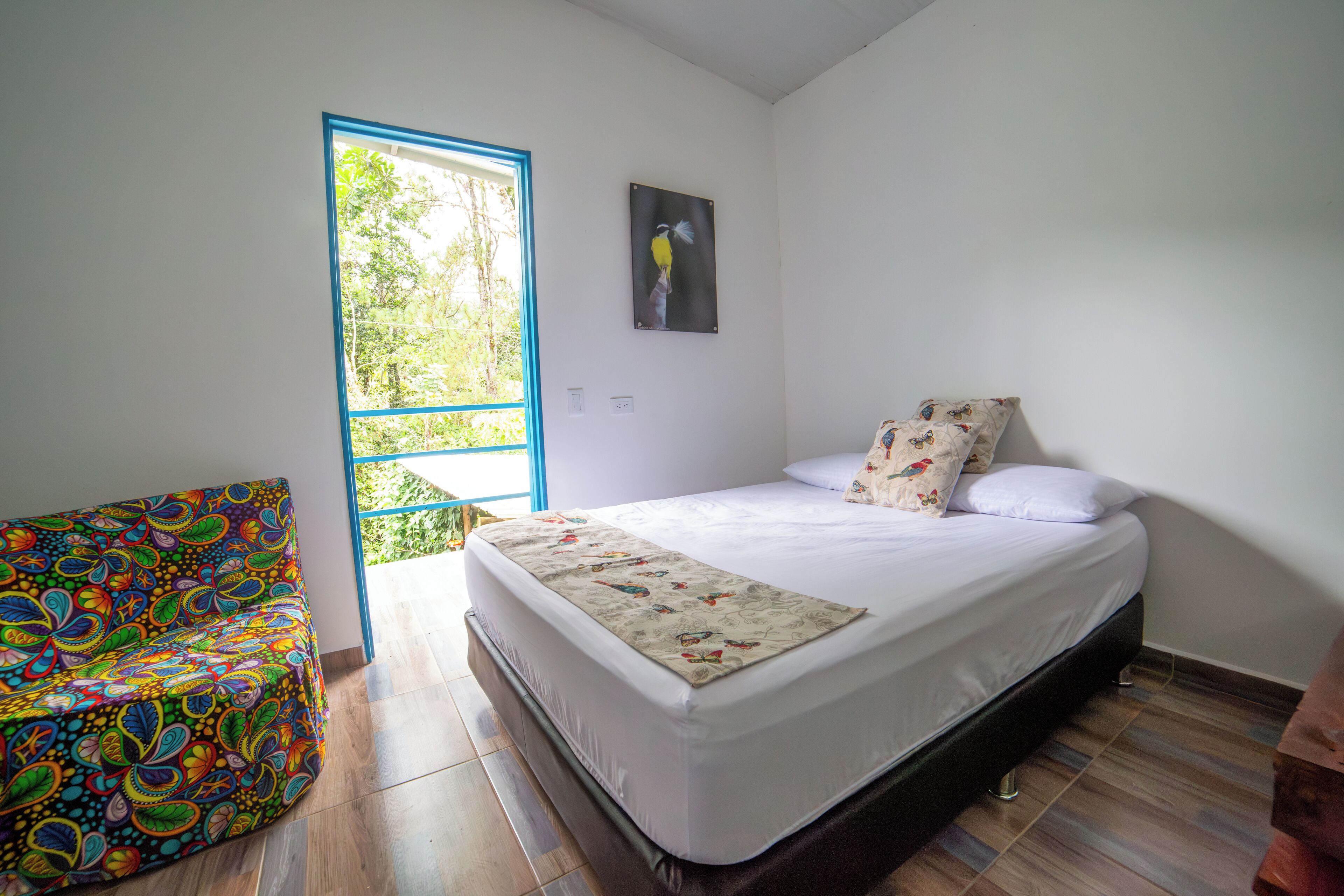 Una camera da letto con un letto, un divano colorato, una finestra con cornice blu e un quadro appeso al muro.