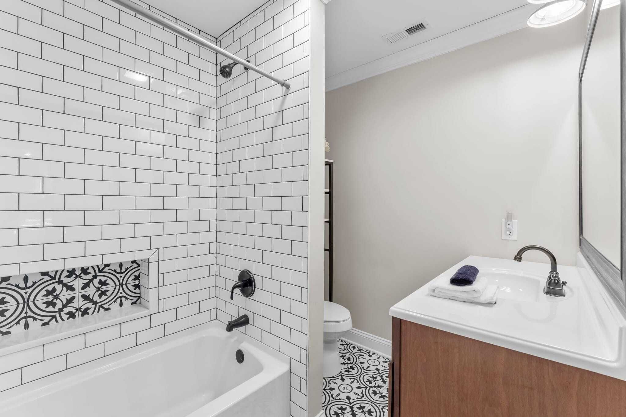 Ein modernes Badezimmer mit weißen Feldbahnböden, einem schwarz-weißen Fliesendeckel, einer weißen Badewanne, einem Waschbecken mit Spiegel und einer Toilette.