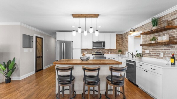A modern kitchen with a central island, stainless steel appliances, and a brick accent wall.