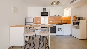 Une cuisine moderne avec un plan de travail en bois, des armoires blanches, un lave-linge encastré et un coin bar avec des tabourets.