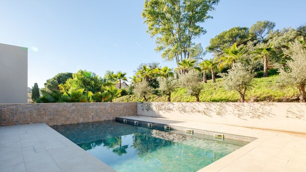 Une piscine rectangulaire à l’eau claire, entourée d’une terrasse carrelée et d’un petit muret en briques.
