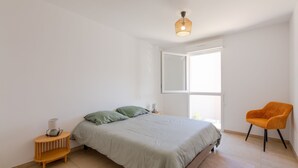 Une chambre à coucher avec un lit, une chaise, une table de chevet et une fenêtre.
