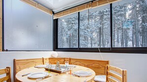 A dining area with a round wooden table set for two, wooden chairs, and a window with a snowy forest view. - Les Lupins - Station de ski à pied (Eyne)