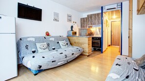 A compact living space with a sofa, a kitchenette, and a wooden door leading to another room. - Les Lupins - Station de ski à pied (Eyne)