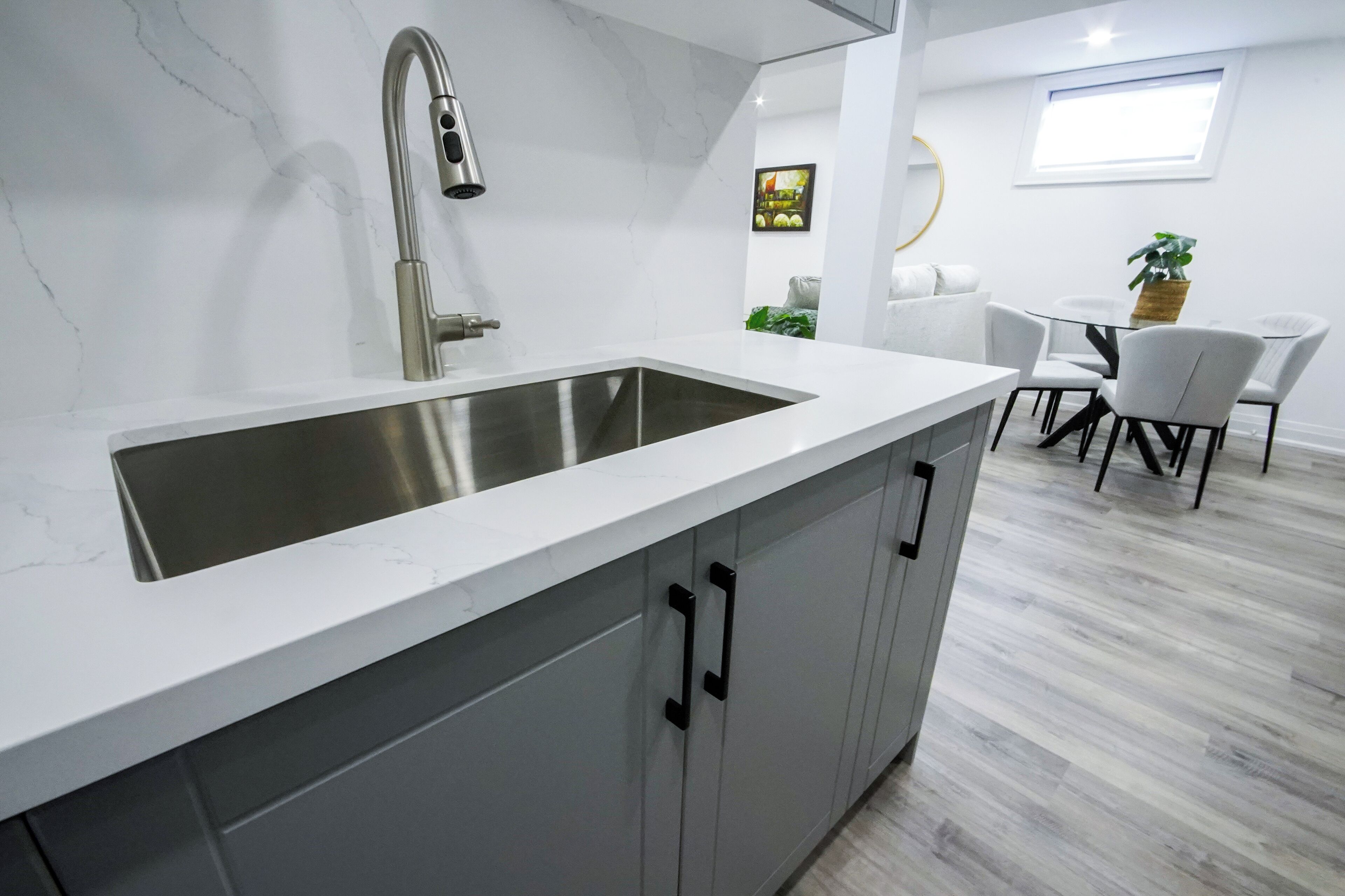 A modern kitchen with a large stainless steel sink, grey cabinets, and a white countertop.