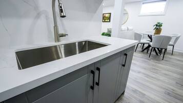A modern kitchen with a large stainless steel sink, grey cabinets, and a white countertop.
