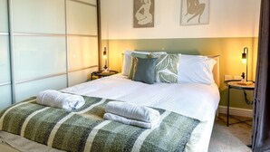 A neatly made bed with a striped blanket and pillows, a bedside table with a lamp, and two wall art pieces depicting a seated figure.