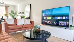 A modern living room with a leather sofa, a glass coffee table, and a flat-screen TV mounted on the wall displaying various streaming services.