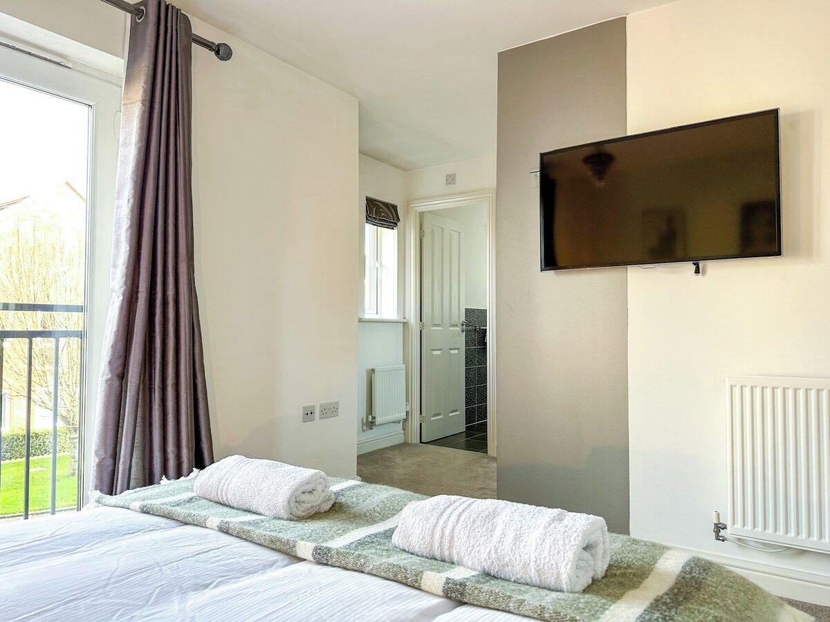 A hotel room with a bed, a flat-screen TV mounted on the wall, and a view of the adjacent bathroom.