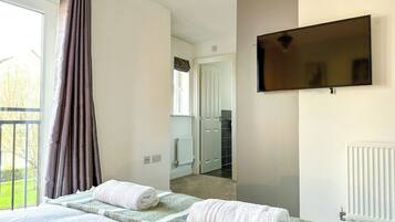 A hotel room with a bed, a flat-screen TV mounted on the wall, and a view of the adjacent bathroom.