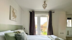 A bedroom with a large bed, a headboard, a chandelier, and a view of the outside through a glass door.