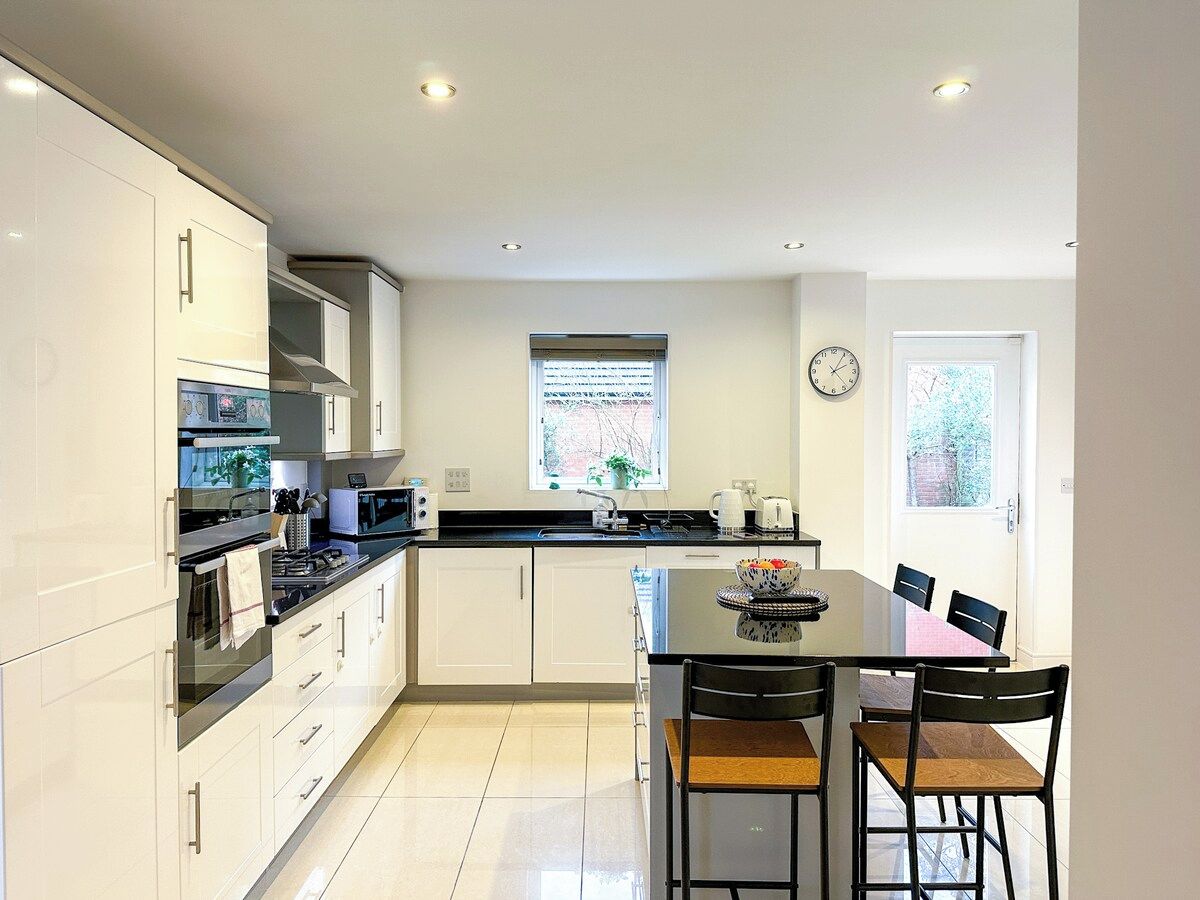A modern kitchen with white cabinetry, a dining table with chairs, and a window with a view of greenery.