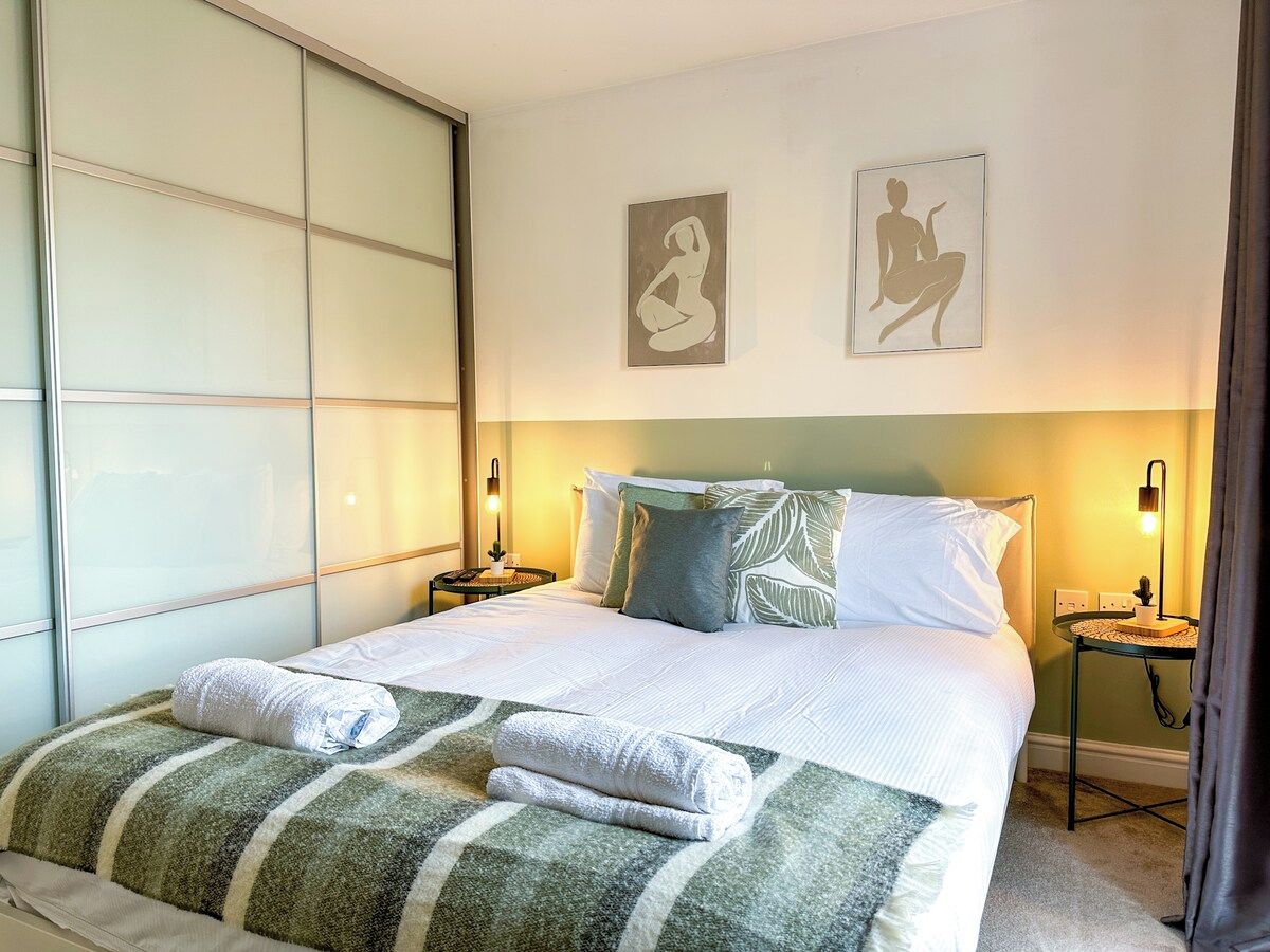 A neatly made bed with a striped blanket and pillows, a bedside table with a lamp, and two wall art pieces depicting seated figures.