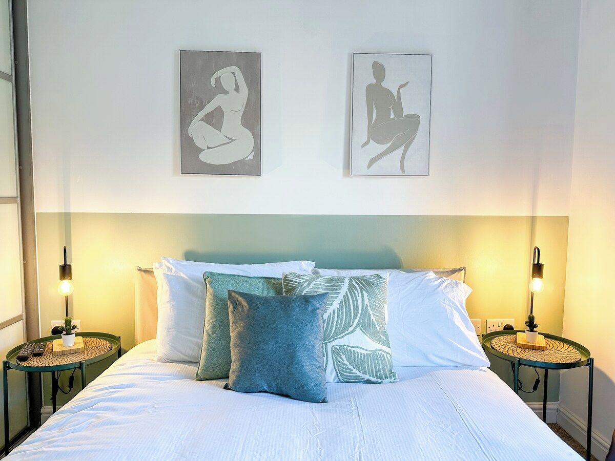 A hotel room with a bed, two bedside tables, a nightstand, a lamp, and two wall-mounted pictures.