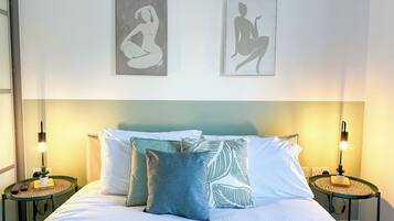 A hotel room with a bed, two bedside tables, a nightstand, a lamp, and two wall-mounted pictures.