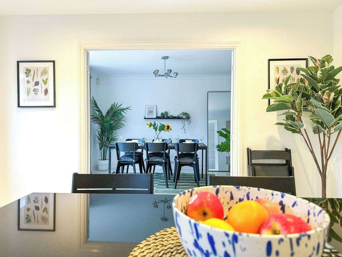 Uma sala de jantar com mesa de vidro, cadeiras e uma cesta de frutas.