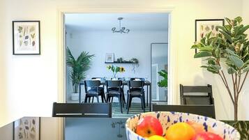 Uma sala de jantar com mesa de vidro, cadeiras e uma cesta de frutas.