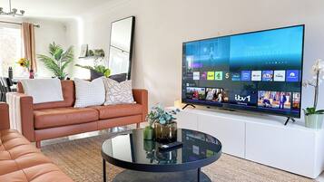 A modern living room with a leather sofa, a glass coffee table, and a flat-screen TV displaying various channels.
