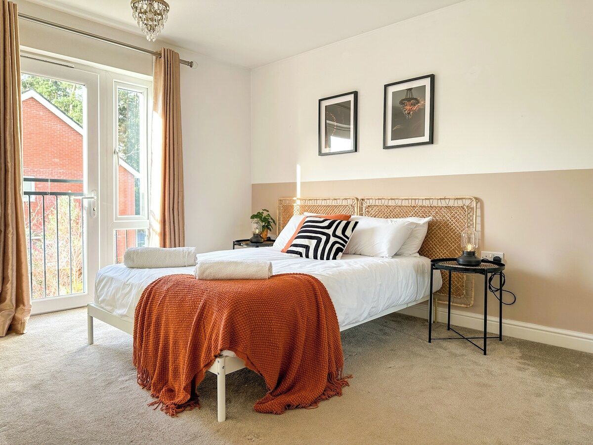 Quarto com cama, mesa de cabeceira, abajur e vista para o exterior.