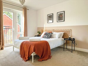 A bedroom with a bed, a bedside table, a lamp, and a view of the outside.