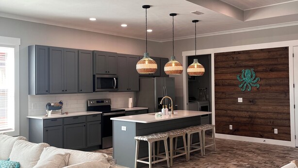 A modern kitchen with grey cabinets, a central island with bar stools, pendant lighting, and a wooden accent wall.