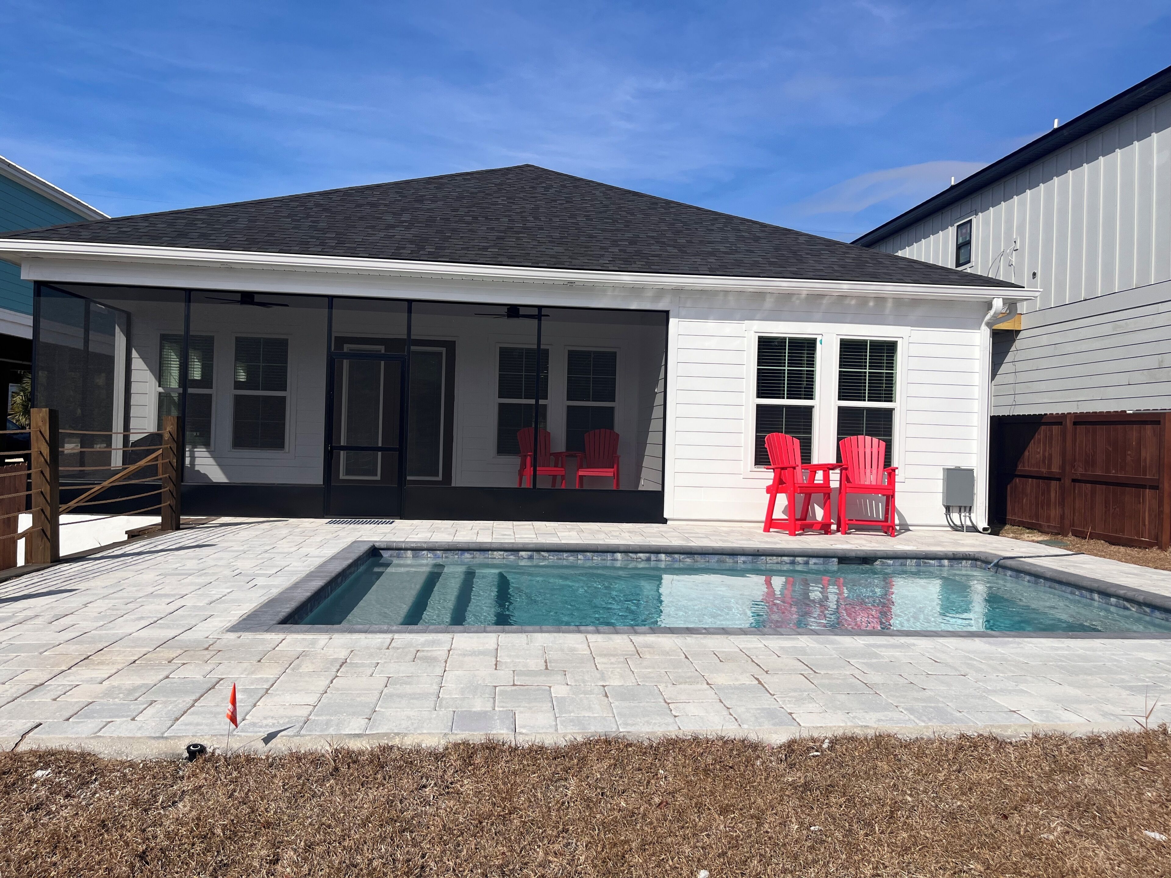 Ein Garten mit Swimmingpool, roten Stühlen und einer überdachten Terrasse.