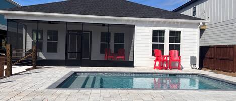Ein Garten mit Swimmingpool, roten Stühlen und einer überdachten Terrasse.