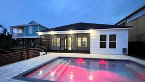 A modern house with a swimming pool, a covered patio, and a neighboring building.